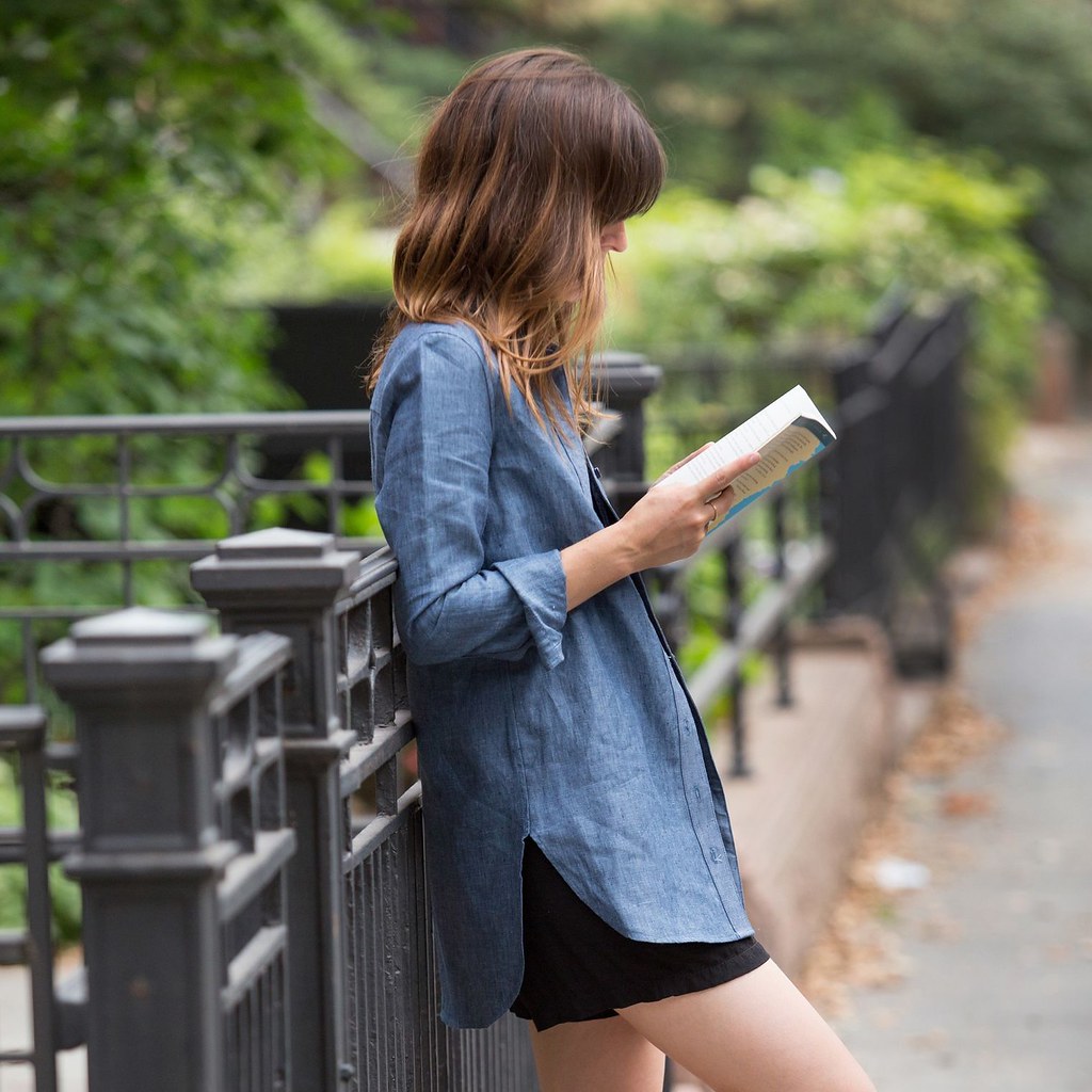 femme qui est entrain de lire dans un parc avec une tunique bleu